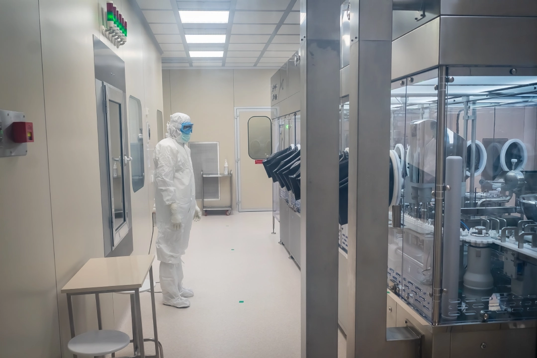 Служител на Антибиотик в стерилно облекло, който следи фармацевтичен производствен процес